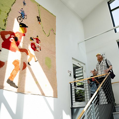 Foto: Anne Schönharting, OSTKREUZ / Ärztekammer Berlin Marlon Wobst vor seiner Filzarbeit „Runtastic” im Treppenaufgang zur Station 1b der DRK Kliniken Berlin Westend