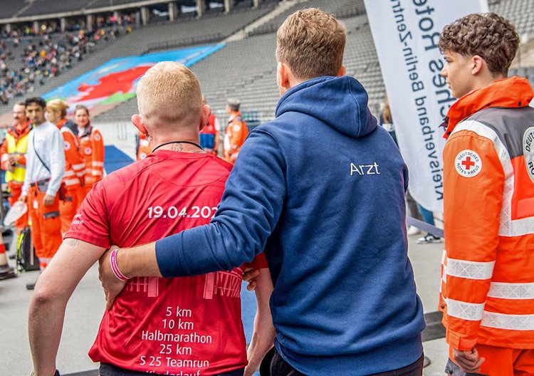 Rennarzt Hartung zusammen mit einem Kollegen vom Roten Kreuz und einem Verletzten Läufer im Olympiastadion Berlin.