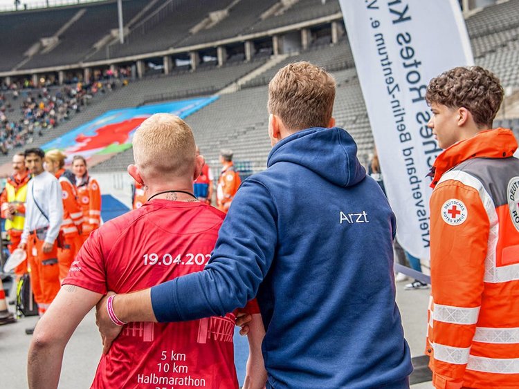 Rennarzt Hartung zusammen mit einem Kollegen vom Roten Kreuz und einem Verletzten Läufer im Olympiastadion Berlin.