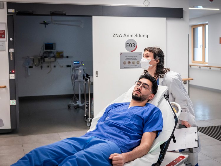 Eine Assistenzärztin bringt den Patienten direkt in den Schockraum, schließt ihn an den Monitor an und untersucht ihn.